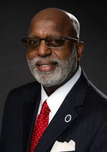 A headshot of Dr. Charles N. Smith, President of the 100 Black Men of Greater Montgomery, wearing a black suit jacket and red tie.